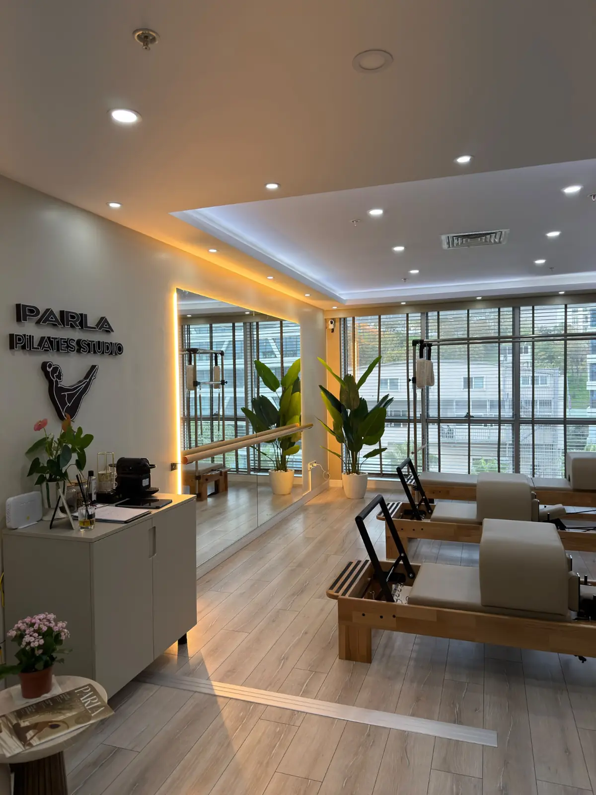 Parla Pilates Studio'da sıralı reformer aletleri, bitkiler ve geniş pencerelerle stüdyonun ikinci görünümü